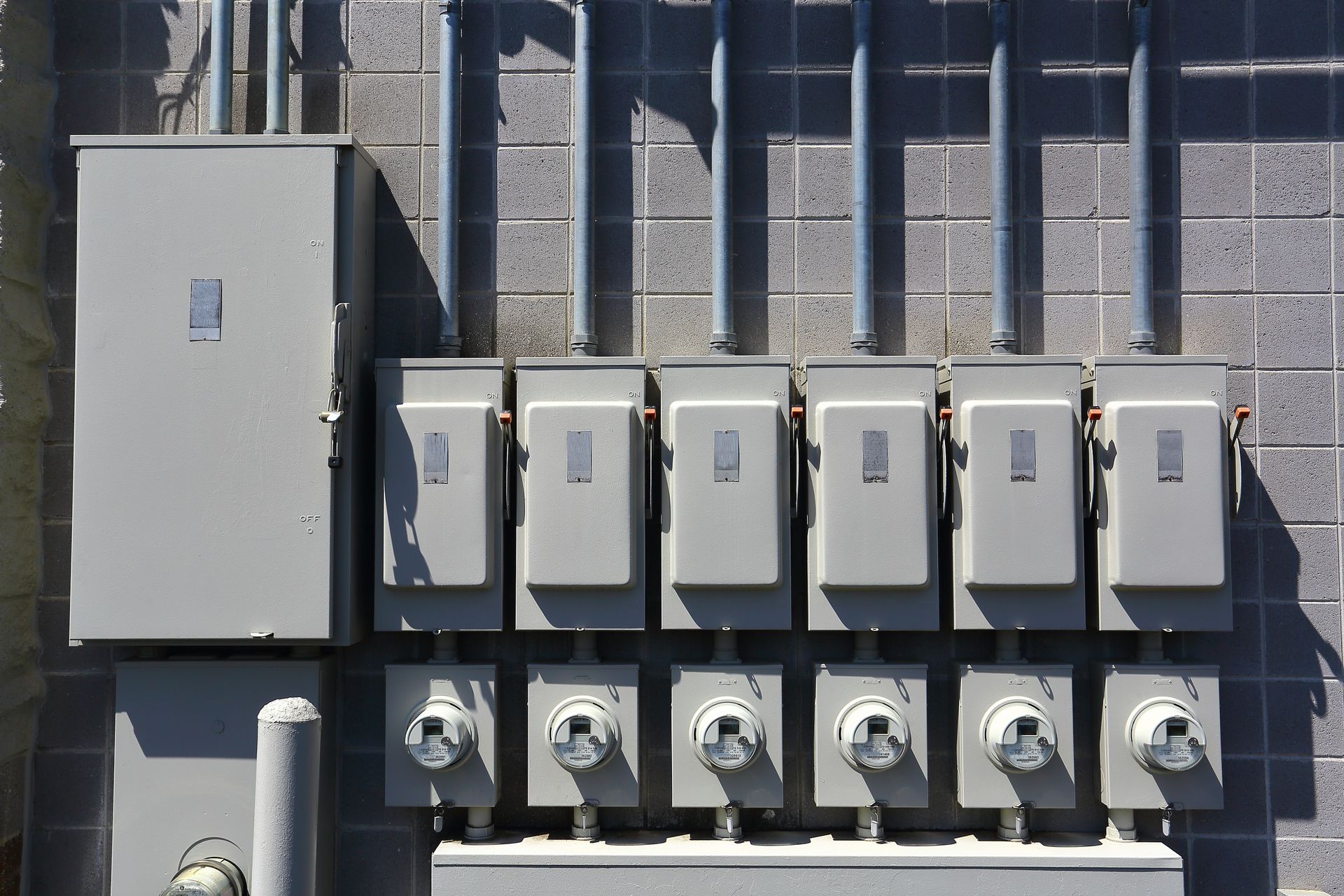 Gray electrical boxes and meters on a brick wall. Metal conduits run vertically.
