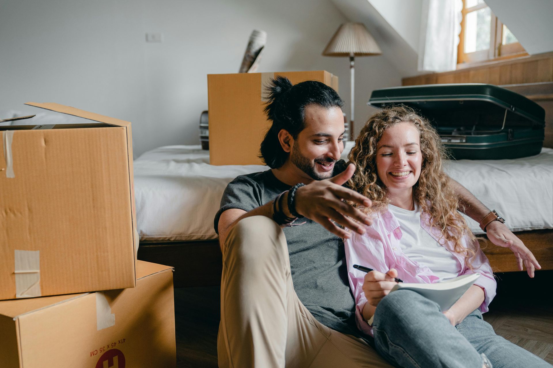 A man and a woman are sitting on the floor in a room with boxes.