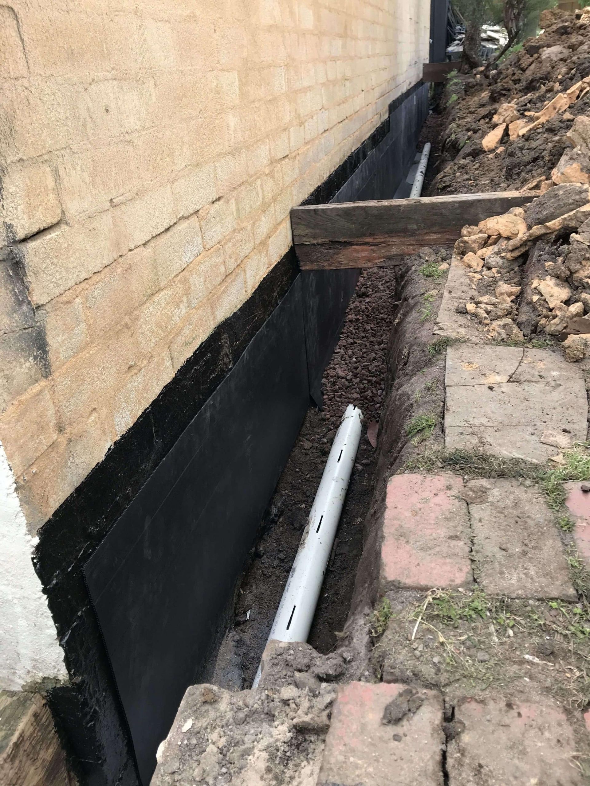 Excavated foundation wall with black waterproofing, drain pipe, and soil.