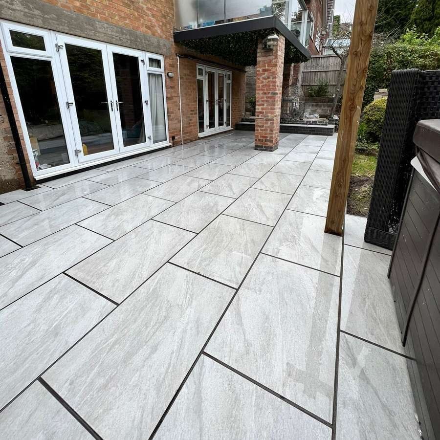 Newly tiled patio, light gray rectangular tiles, bordered in black, leading to house with French doors.