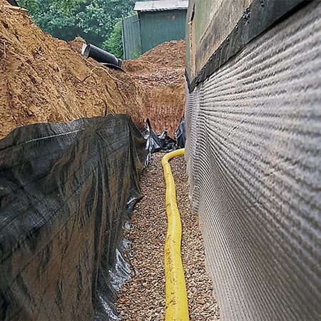 Two-story brick house with white gravel driveway, gray garage doors, and a blue sky.
