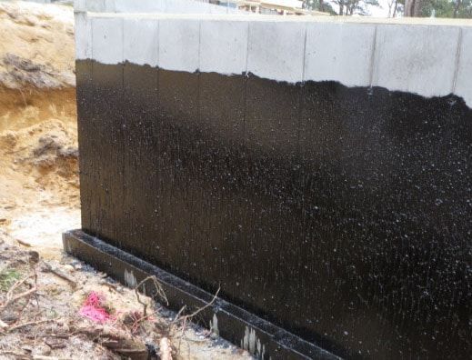 Black waterproofing sealant applied to a concrete foundation wall during construction.