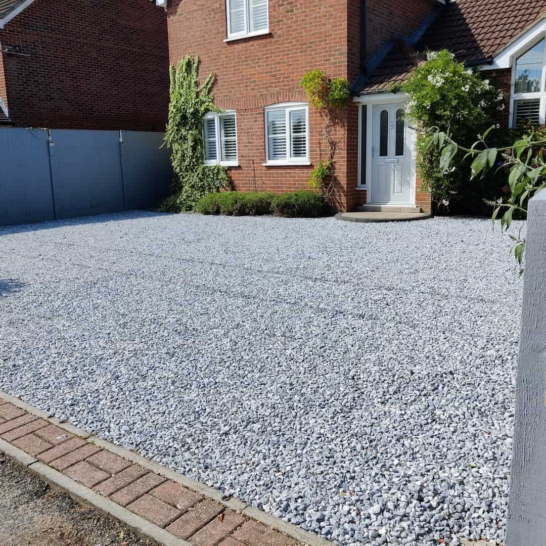 Gravel driveway in front of a brick house with white trim and door.