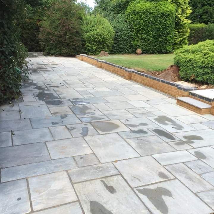 Stone patio leading toward a manicured lawn with hedges and bushes.