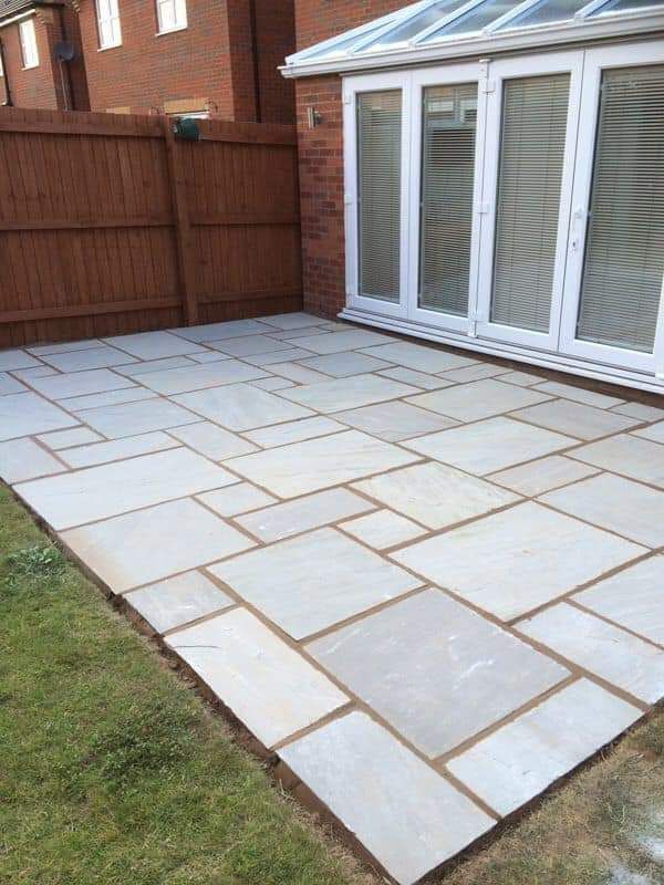 Stone patio leading toward a manicured lawn with hedges and bushes.