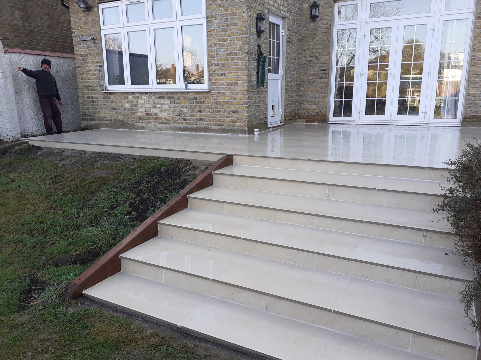 Exterior shot: tiled steps leading up to a house with large windows and a man painting a wall.