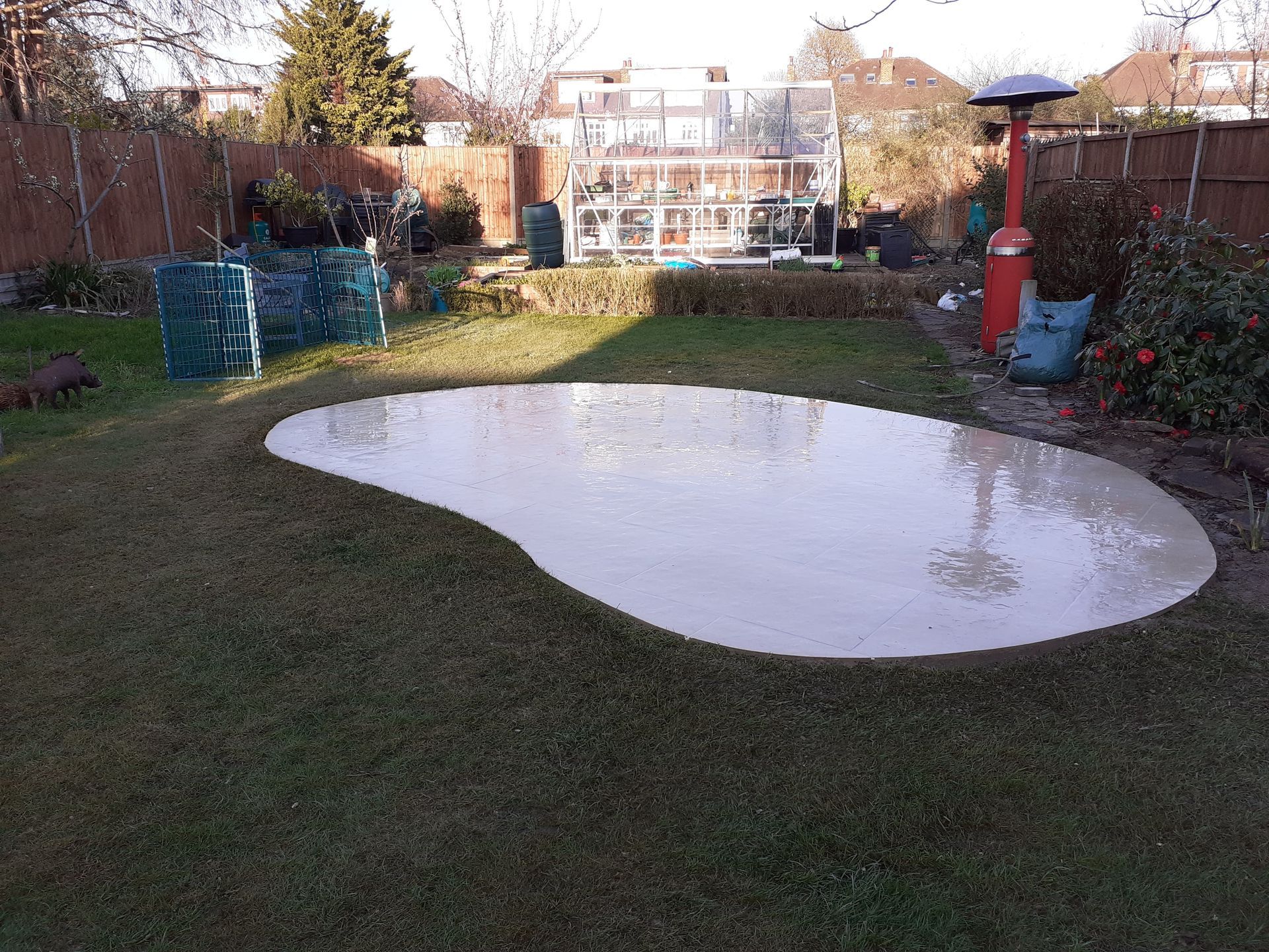 A large, empty pond in a grassy backyard. The pond has a light colored lining.