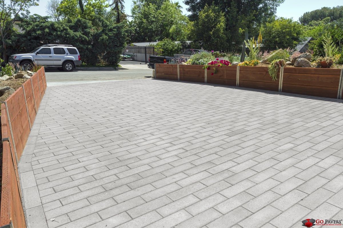 Brick paved driveway with wooden planters overflowing with flowers. SUV parked on the left.
