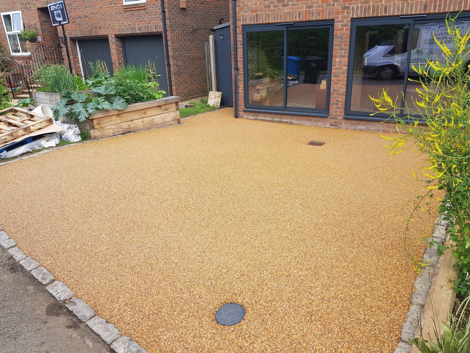 Gravel driveway with a brick house in the background. A few plants and a small wall border the driveway.