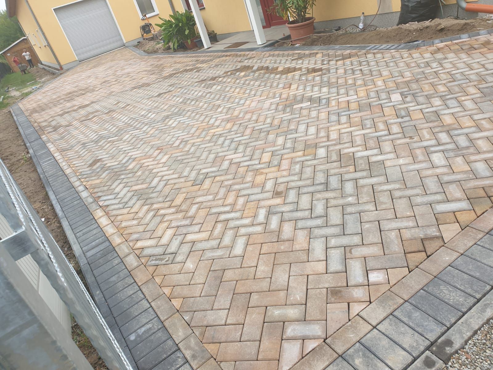 Herringbone pattern brick driveway leading to a garage. Borders are dark gray.