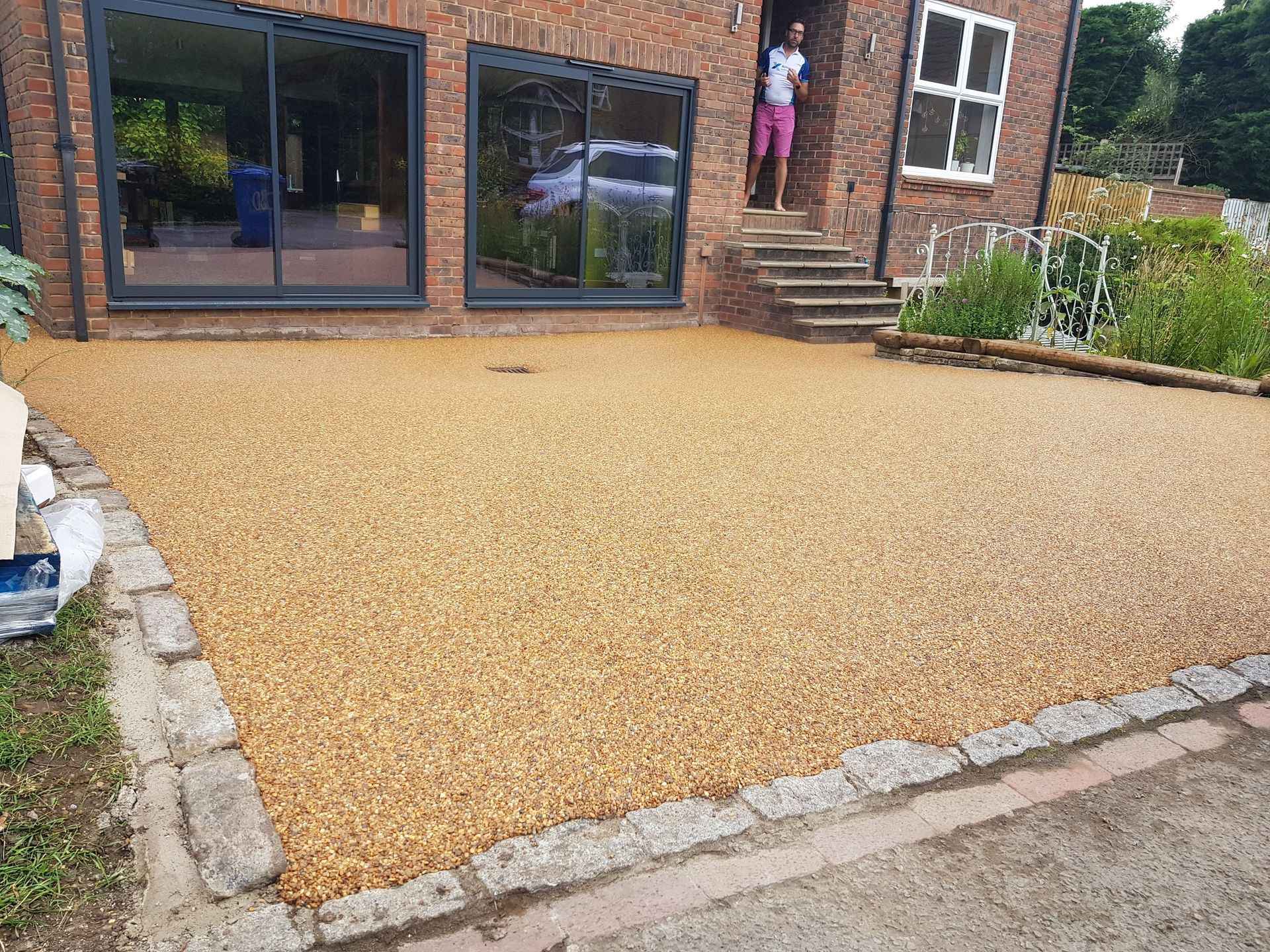 Gravel driveway with brick house, a person standing by the front door, and stone bordering the driveway.