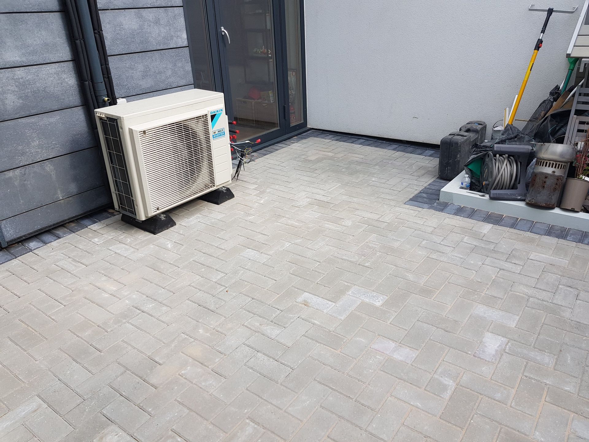 Air conditioning unit outside on a light gray brick patio.