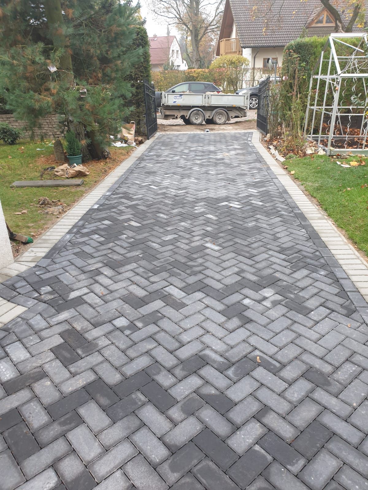Herringbone pattern brick driveway leading to a gate, with a truck visible in the background.