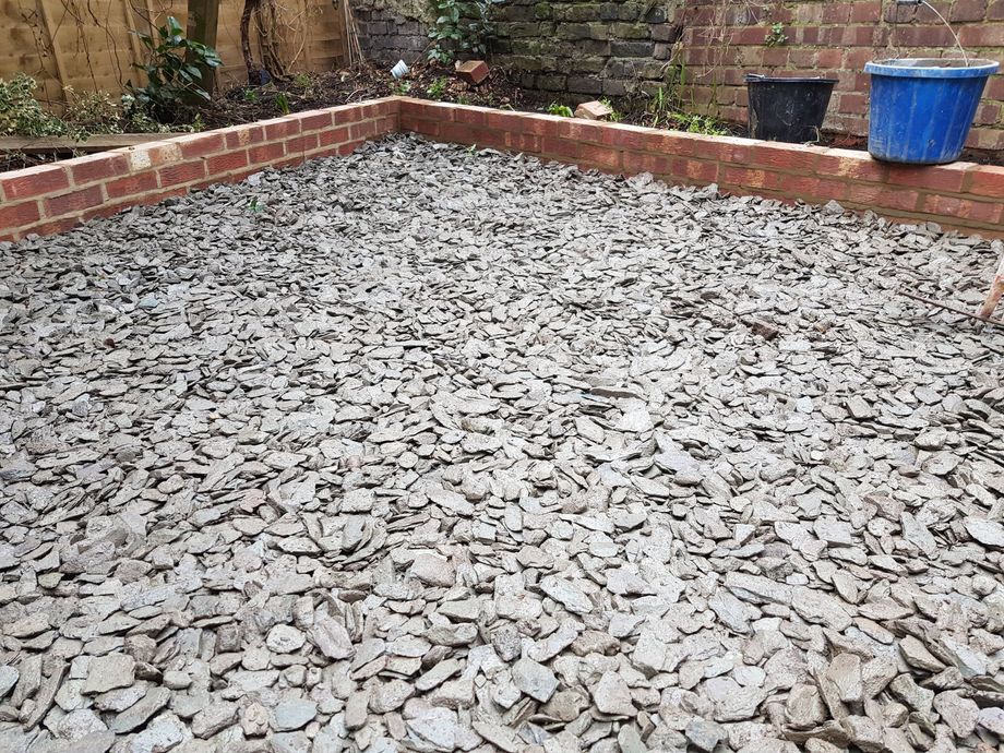 Gravel driveway with a brick house in the background. A few plants and a small wall border the driveway.