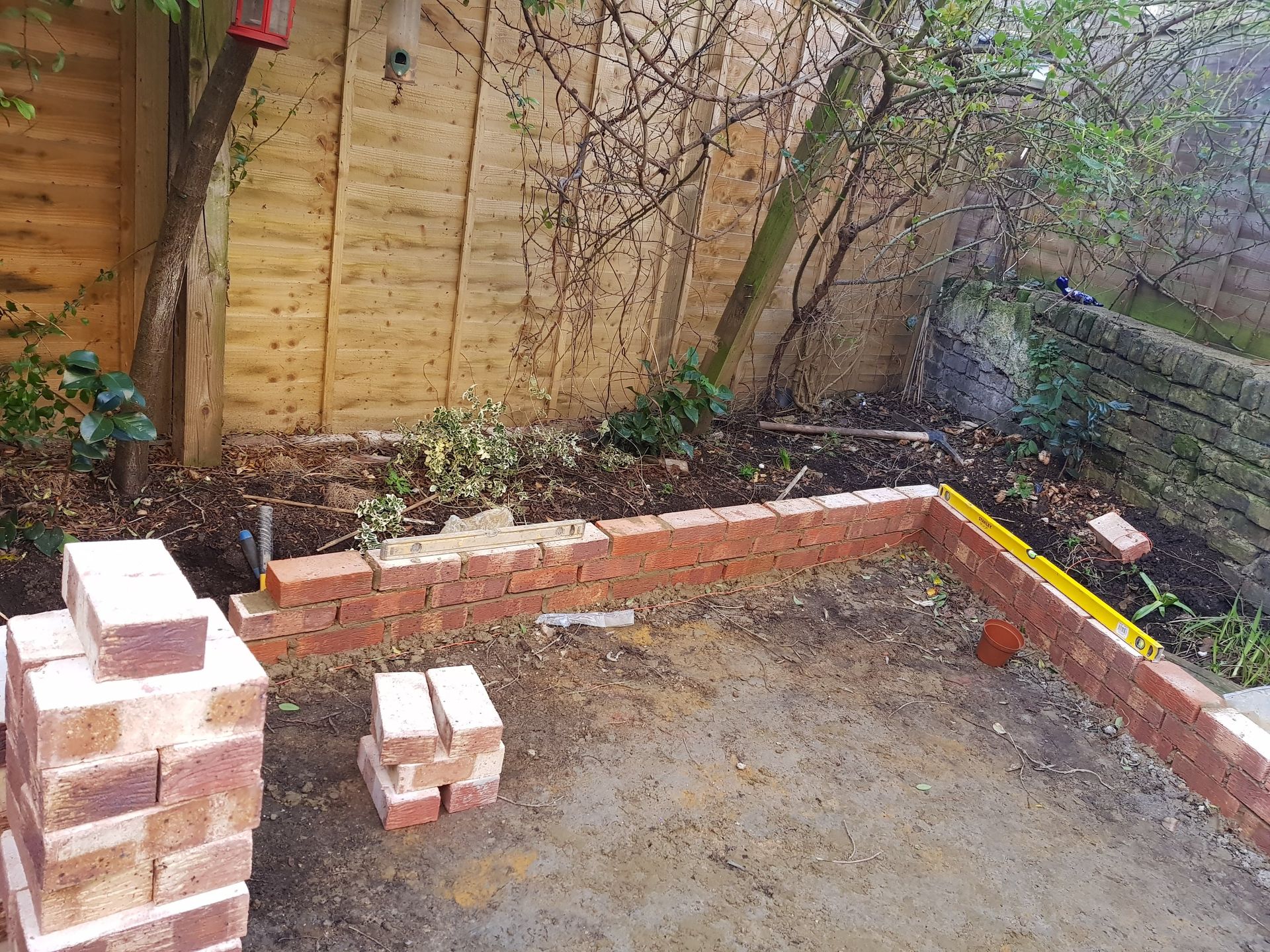 Newly paved patio with grey and beige bricks, leading to a gravel pathway, tools on left.