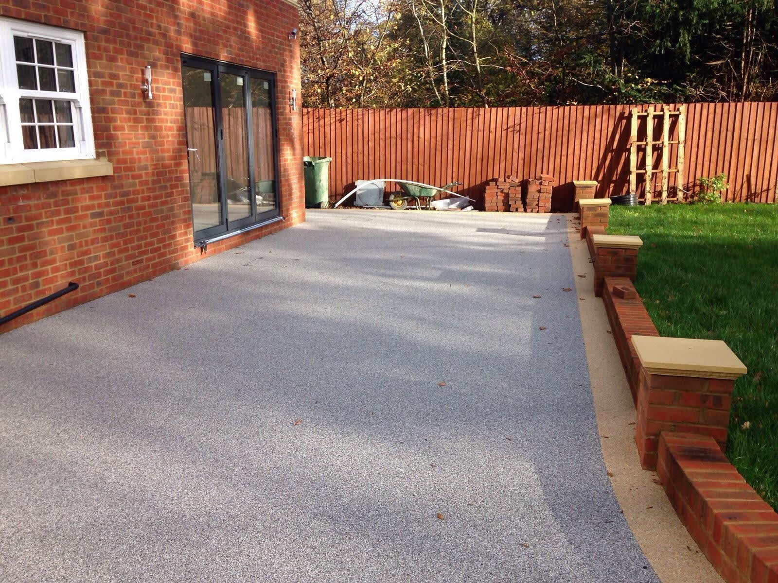 Exterior patio with grey aggregate surface, brick walls, and a red fence.