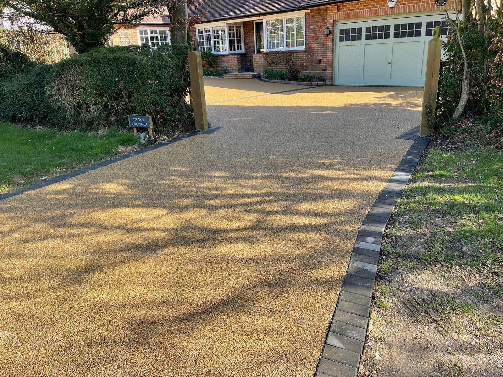 Gravel driveway leading to a brick house with green garage doors. Edged with dark brick.