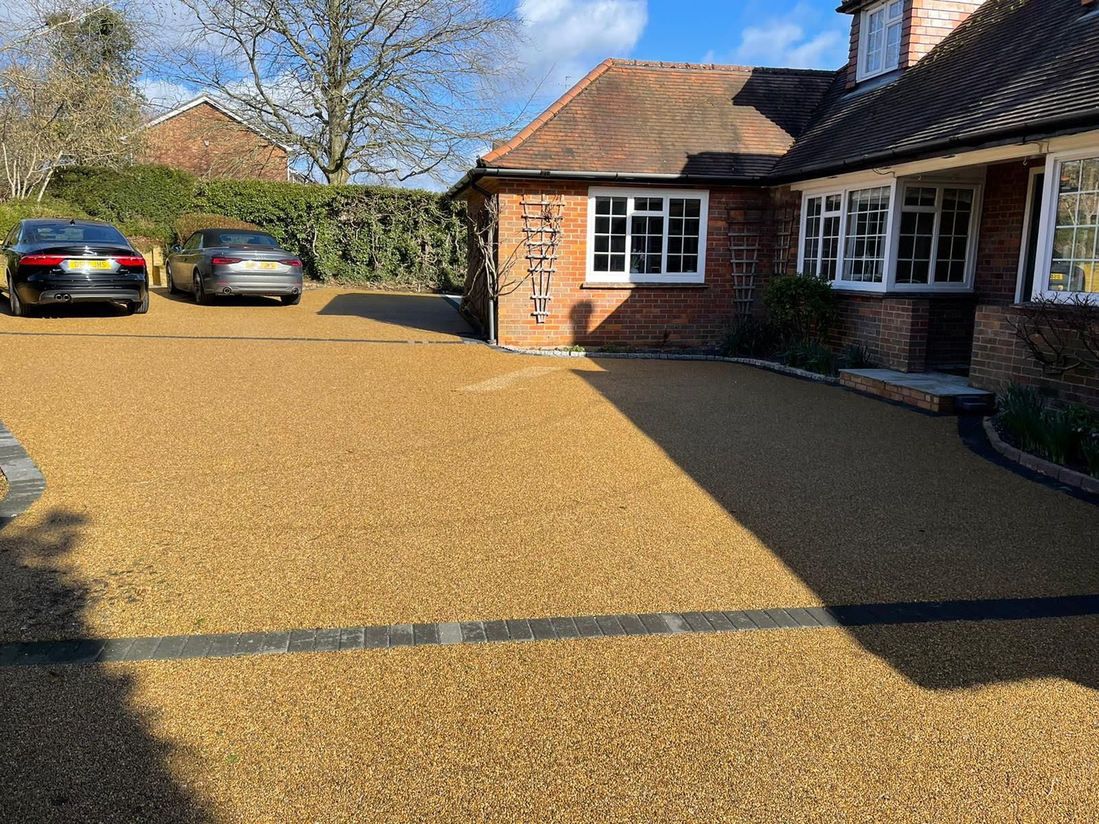 A gravel driveway in front of a red brick house with two cars parked. Sunny day.