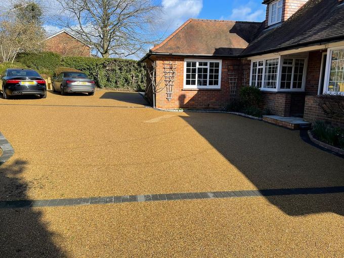 Gravel driveway in front of a brick house, two cars parked, sunny day.