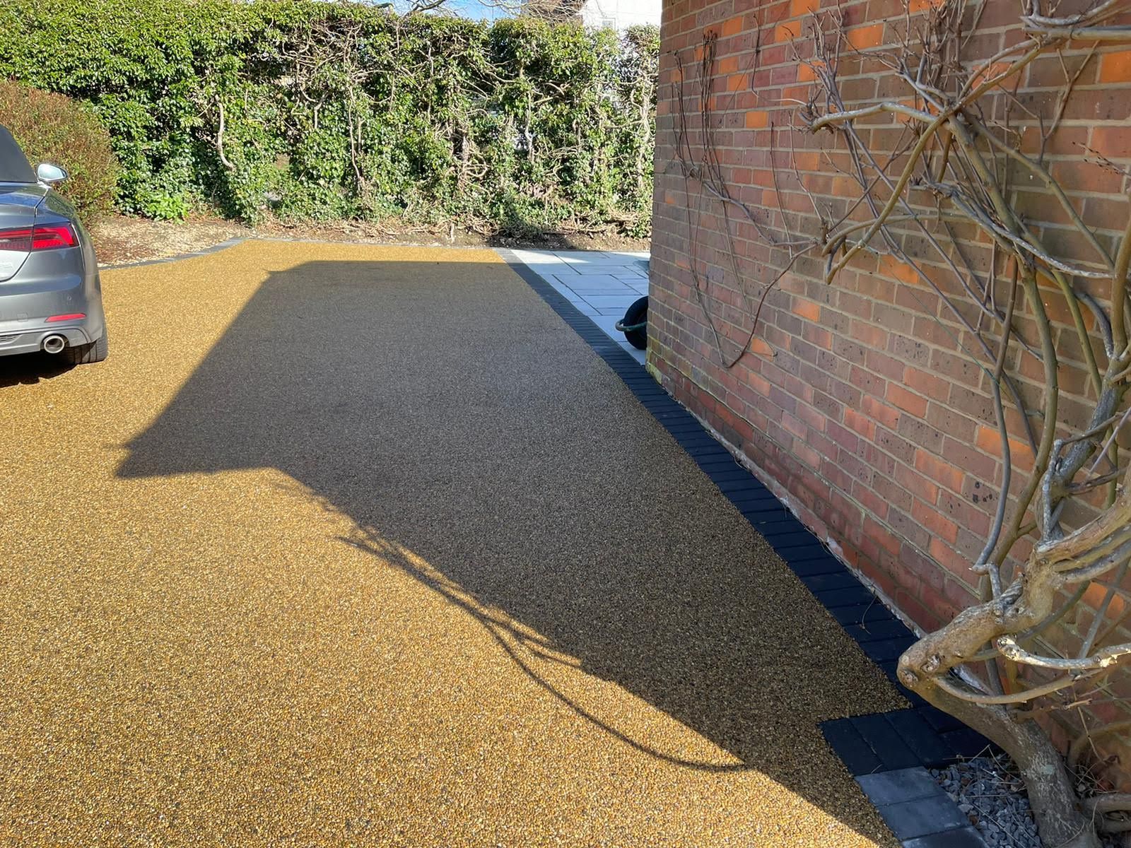 A gravel driveway with a car parked on the left next to a brick wall with climbing vines.