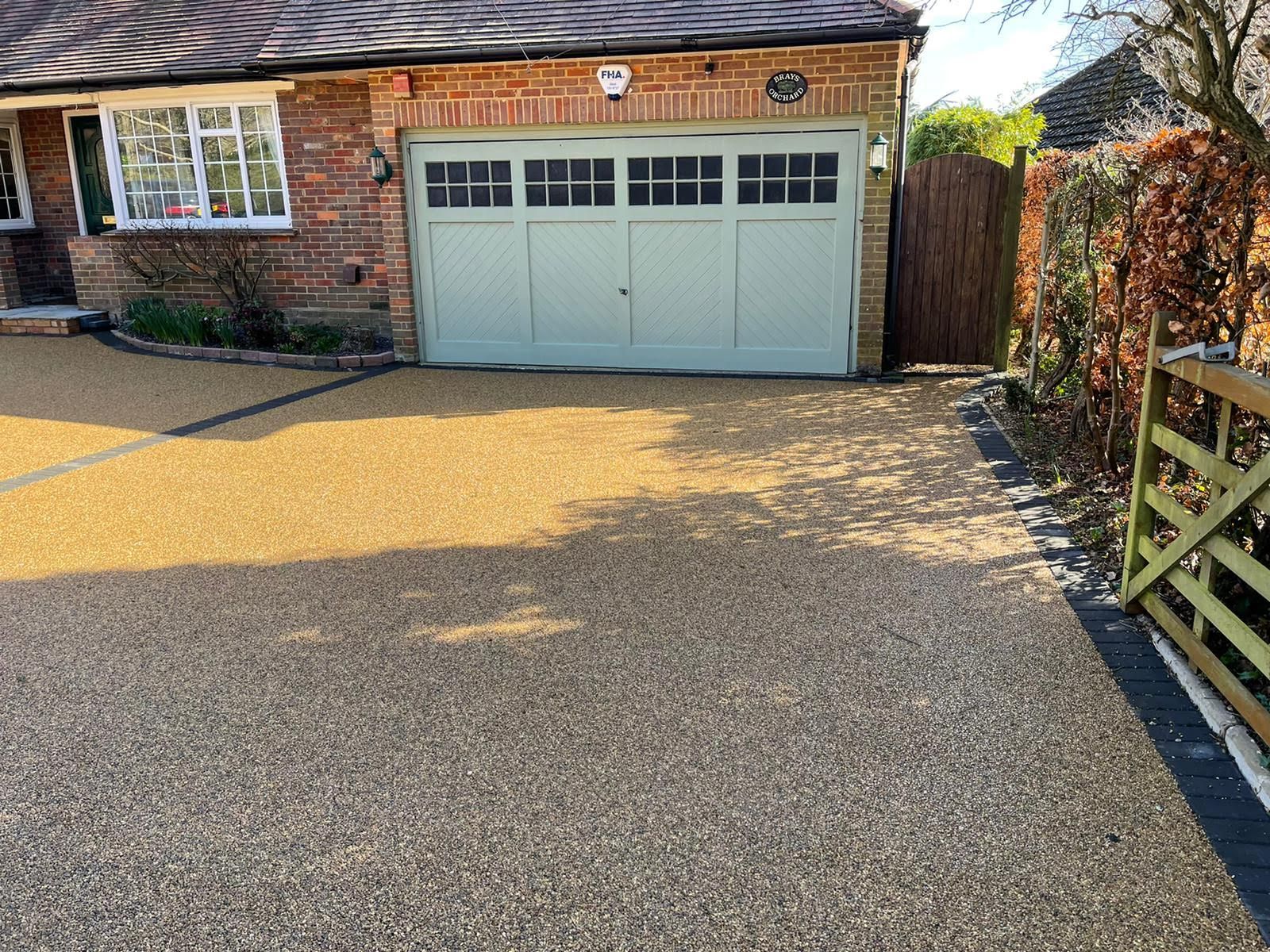 Gravel driveway leading to a brick house with a green garage door and a wooden gate.