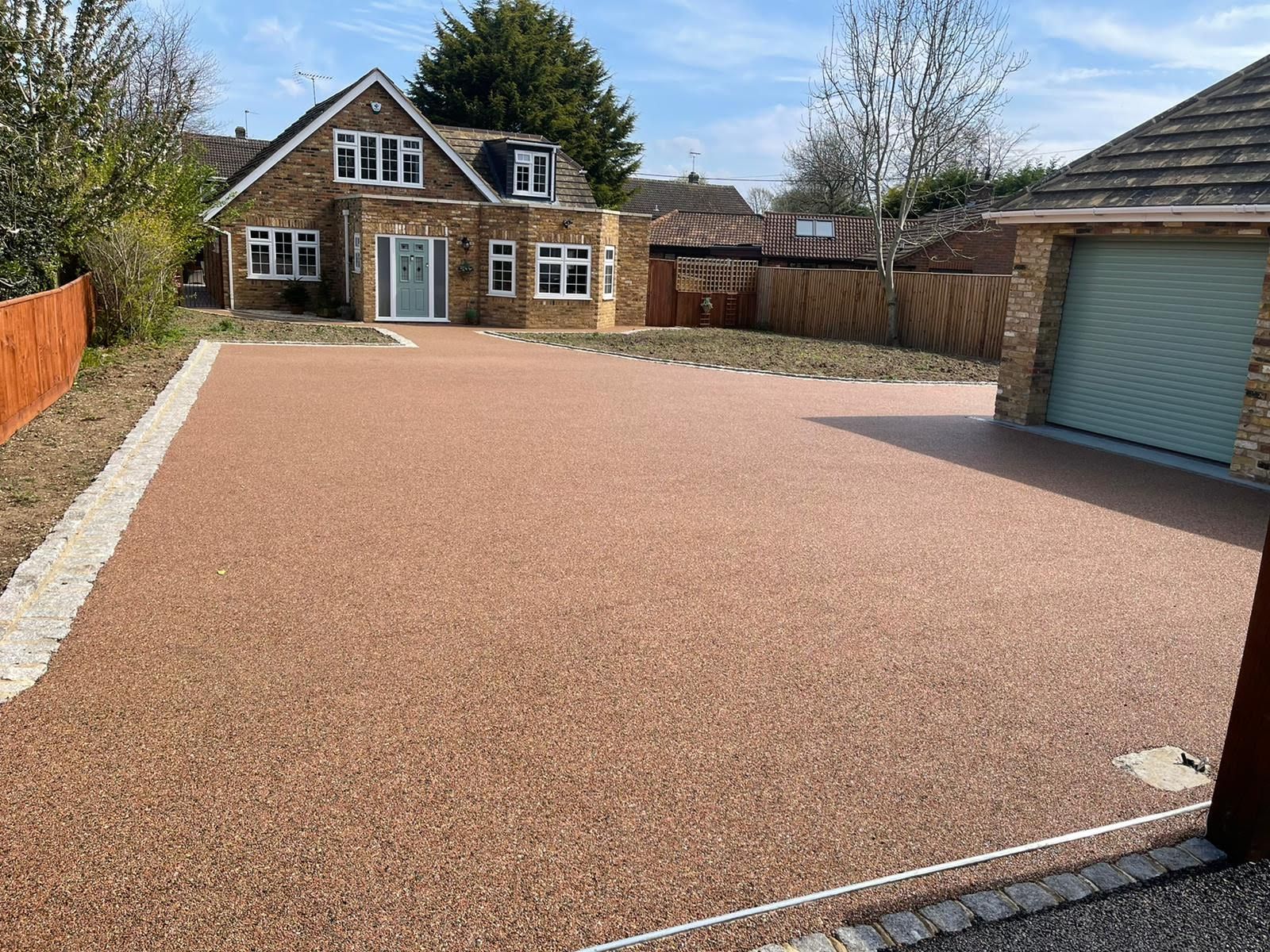 Brown resin driveway in front of a beige brick house with a garage. Sunny day.