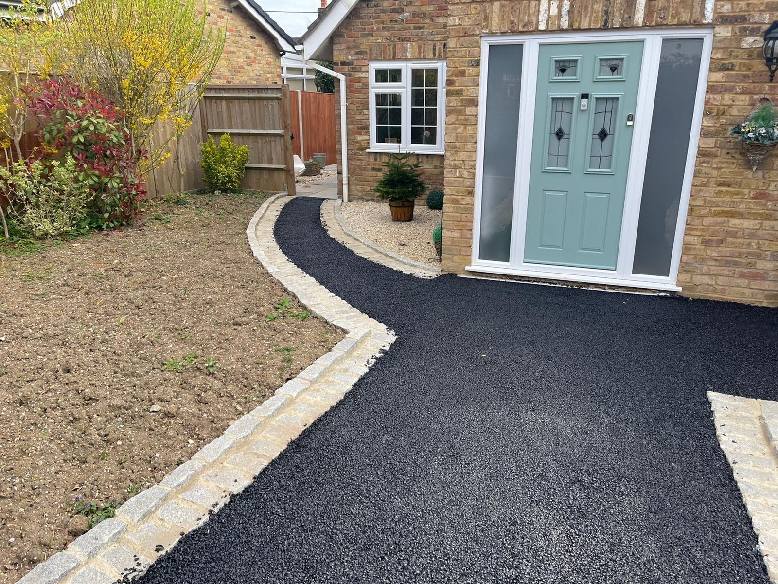 Driveway with black gravel, bordered by tan paving stones, leading to a teal door.
