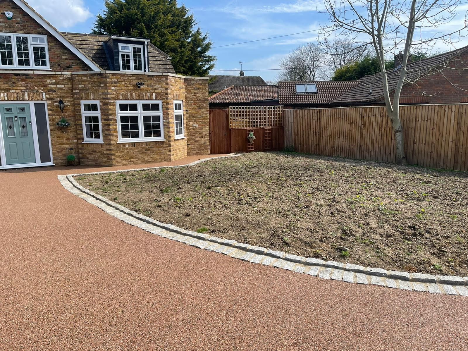 House with red driveway, dead grass lawn, and wooden fence.