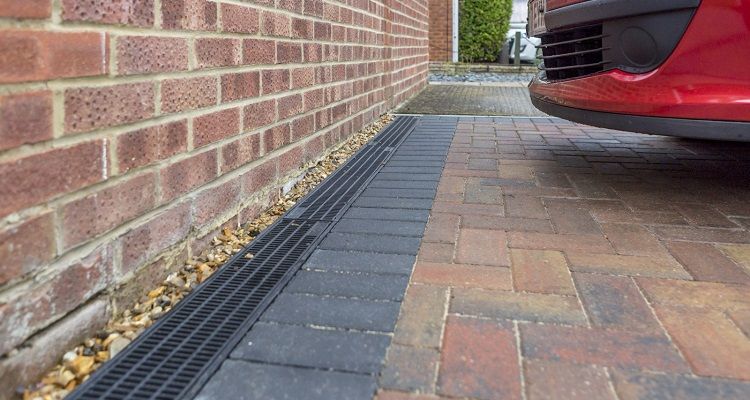 Brick wall next to a driveway with a drainage channel and a red car.