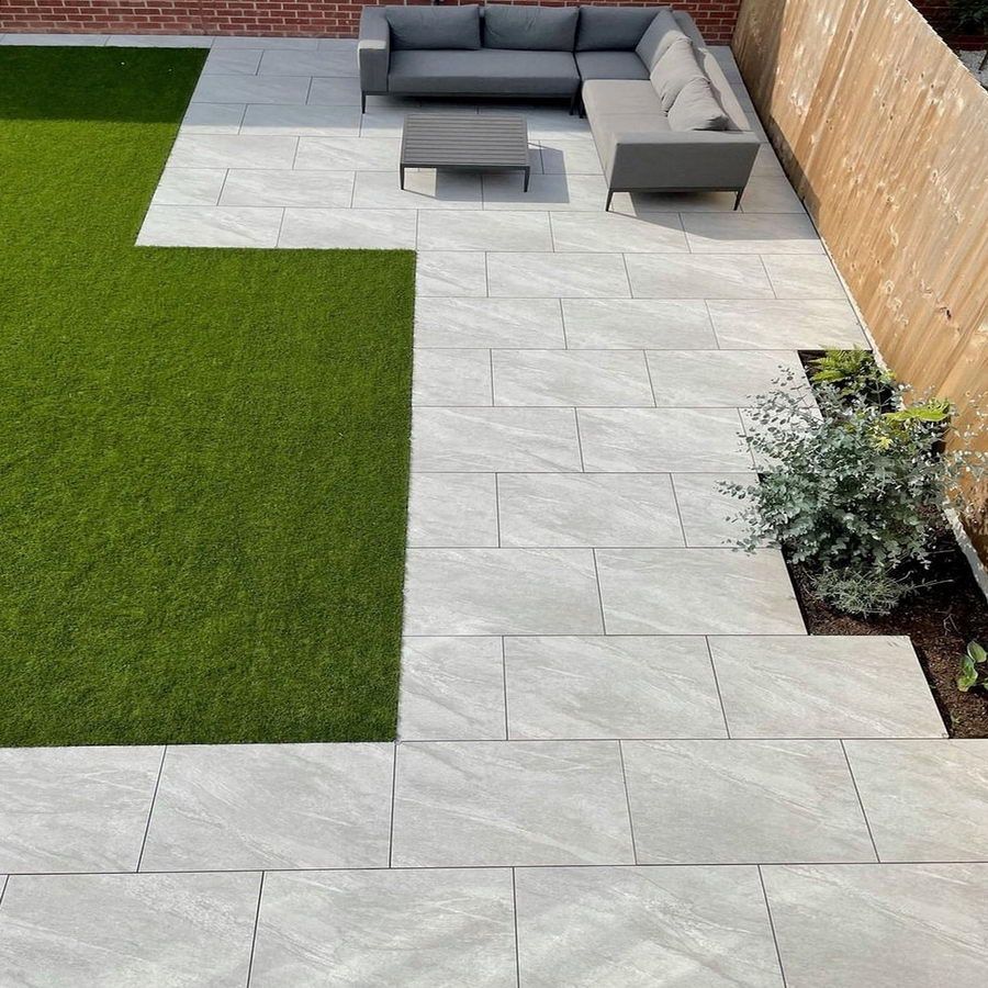 Patio with light gray rectangular pavers, gray sectional sofa, and artificial grass.