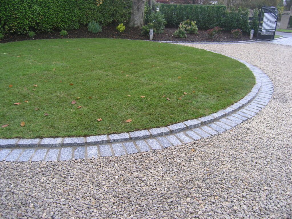 Stone patio leading toward a manicured lawn with hedges and bushes.