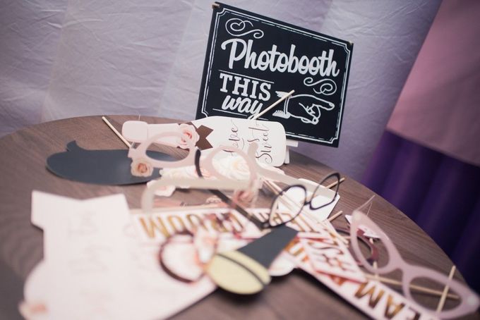 A chalkboard sign pointing to a photobooth, set on a table covered in assorted paper photo props.