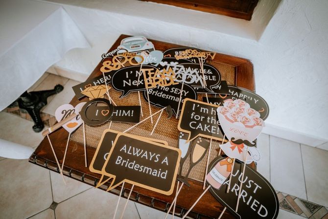 A collection of wedding-themed photo booth props with signs and illustrations on sticks sitting on a wooden table.