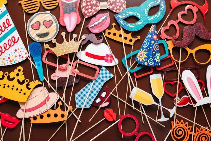 A collection of colorful photo booth props on sticks, including masks, hats, crowns, glasses, lips, and festive decorations.