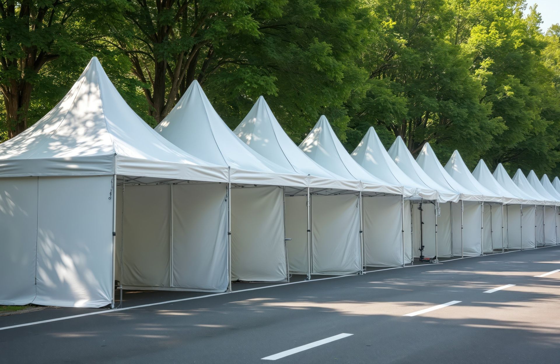 Row of white event tents lining a tree-shaded roadside