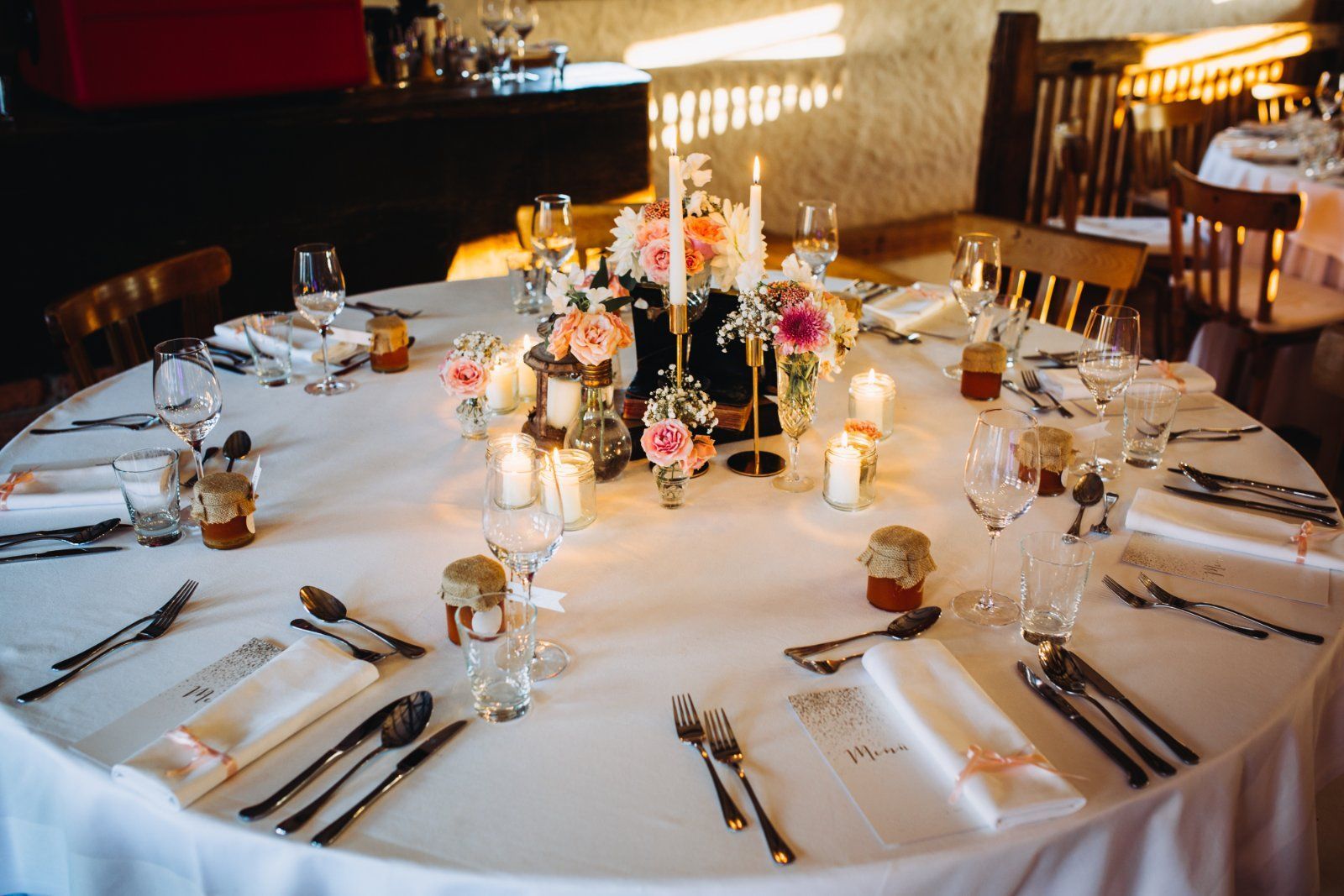 A round table set for a formal event with white linens, floral centerpieces, candles, and place settings.