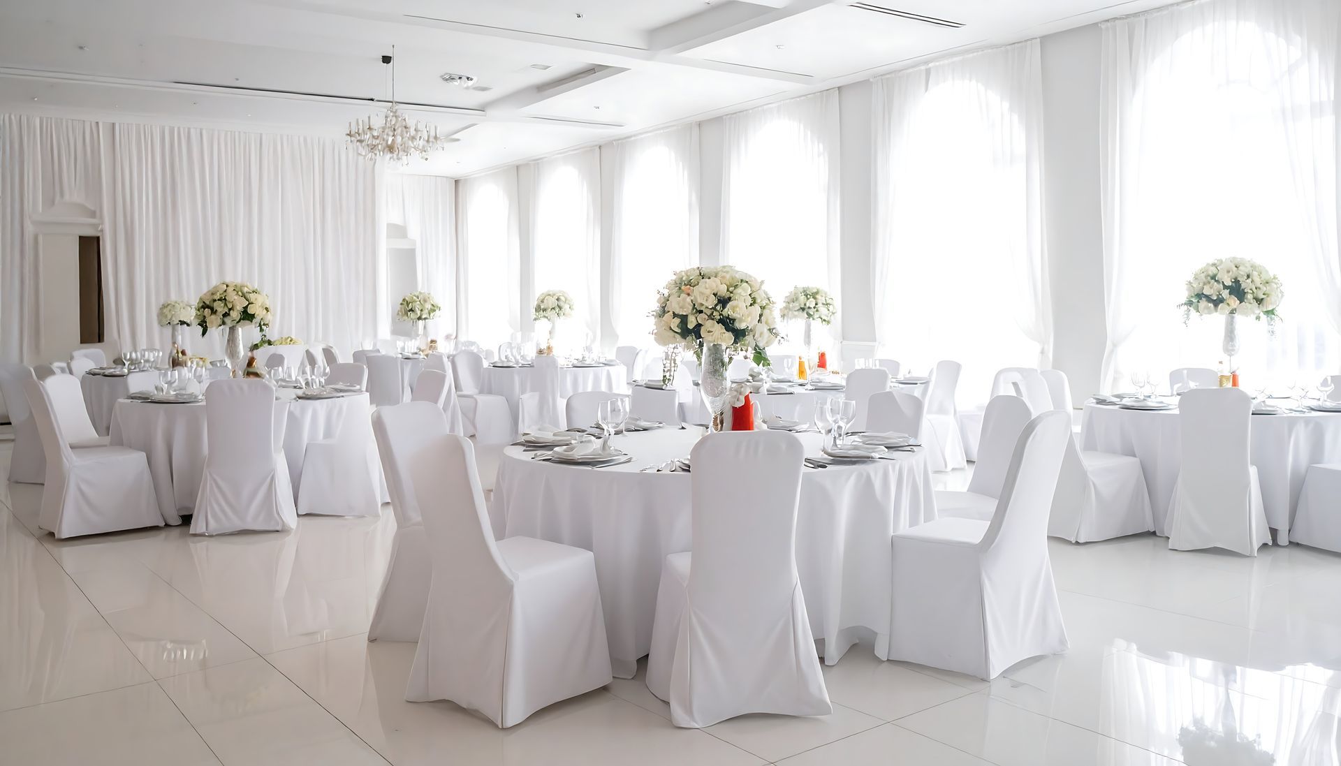 Bright white banquet hall with round tables, white chair covers, and floral centerpieces