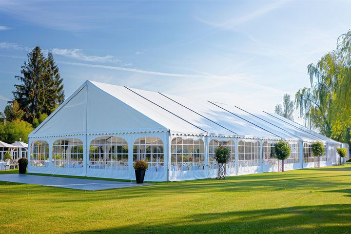A large white event tent with arched windows standing on a green lawn against a blue sky.