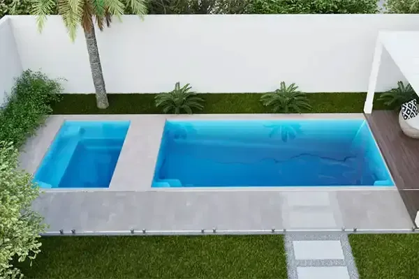 Modern backyard pool with blue water, small spa, and a white patio beside green lawn and plants