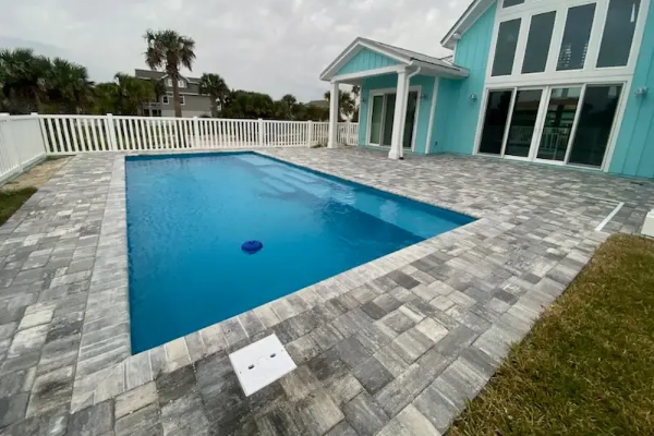 Modern backyard with a blue swimming pool beside a turquoise house and gray stone patio