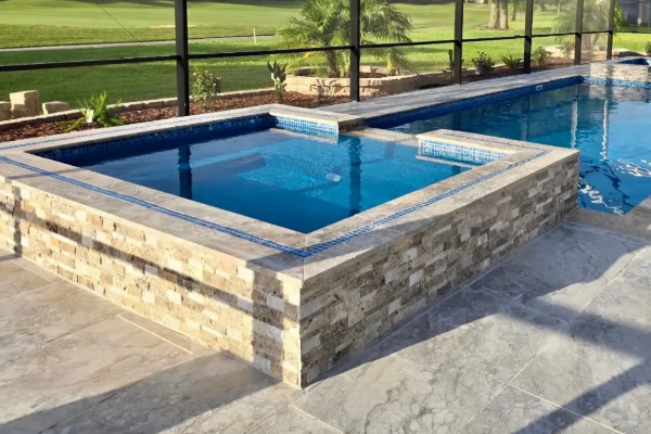 Stone-lined outdoor pool with blue water beside a patio and grassy field