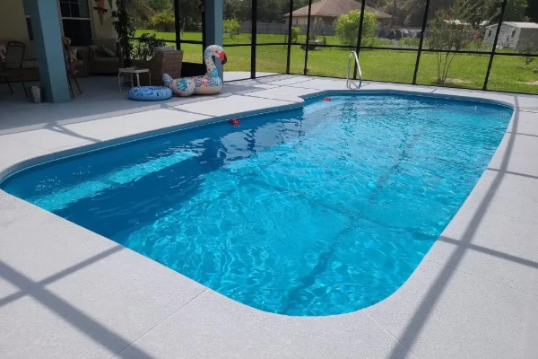 Backyard swimming pool with bright blue water, white deck, and screened enclosure and patio furniture nearby