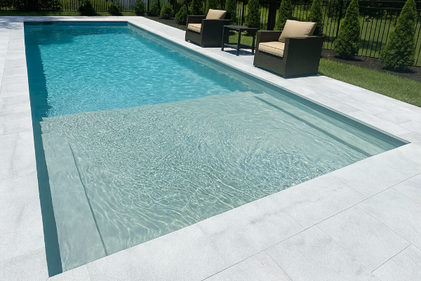Modern rectangular backyard pool with clear blue water, white stone deck, and lounge chairs at the far end