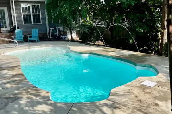 Backyard swimming pool with turquoise water beside a patio and house.