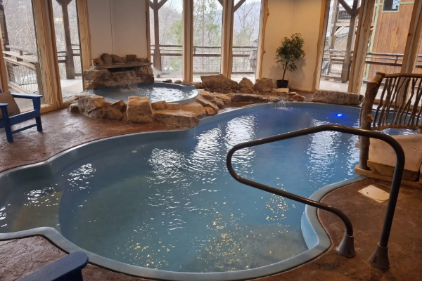Indoor spa pool with rock waterfall, hot tub, and large windows in a sunlit room