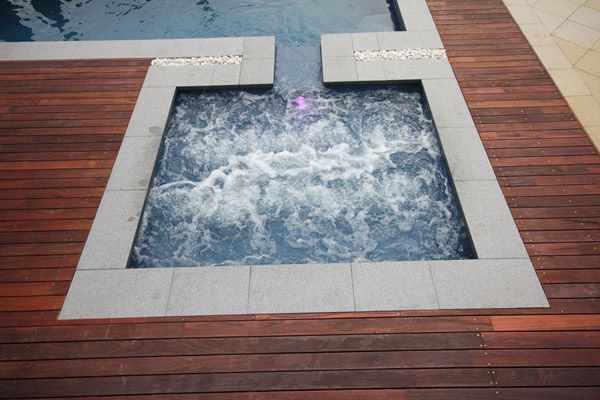 Wooden deck with a square bubbling hot tub and blue water jets
