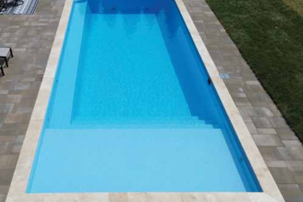 Rectangular backyard swimming pool with clear blue water and stone patio edges