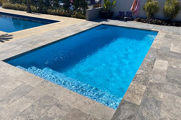 Rectangular backyard swimming pool with bright blue water and stone patio surround