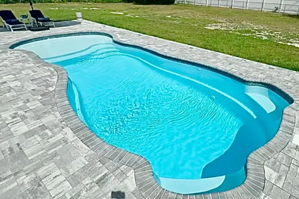 Curved backyard swimming pool with bright blue water and gray stone patio