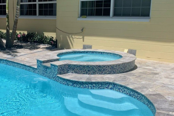 Backyard swimming pool with a raised spa and tiled steps beside a house